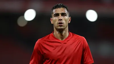 A mid-30s anonymous Rodez midfielder, wearing a solid red jersey, captured waist-up with a focused expression, background...