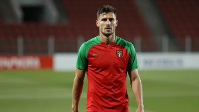 A determined, athletic Rodez player, mid-20s, with a strong build, wearing a plain red and green training top, fills the...