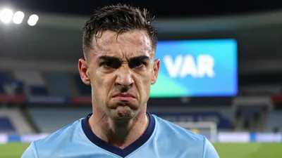 A close-up shot of a Rodez player looking frustrated and angry on the pitch, with a VAR screen in the background