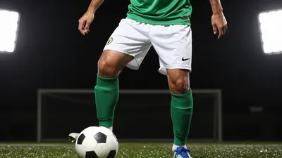 A photorealistic image of a Rodez player, wearing a green jersey and white shorts, with a white ball at his feet, taken...