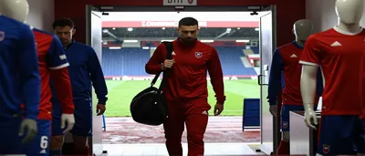 A hyper-realistic editorial shot of a young midfielder in a plain red jersey sprinting across a rain-slick Ligue 2 pitch...