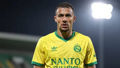 A 30-year-old FC Nantes player, with a muscular build, in a yellow and green jersey, looking concerned, with a shallow...