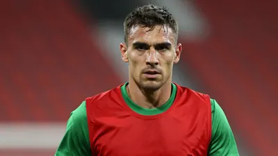Mid-30s rugged forward, muscular torso, intense eyes, head-and-shoulders shot, wearing a plain red and green training top...