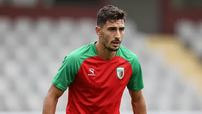 A determined, athletic Rodez midfielder, 25, with a strong build, wears a plain red and green training top, soft natural...