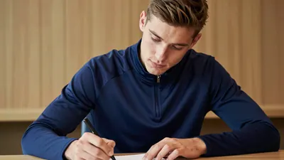 25-year-old athletic full-back, lean build, signing a contract at a desk, wearing a solid navy blue training top, warm...