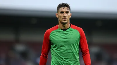 Mid-30s rugged midfielder, athletic build, waist-up, face intense and centered, wearing a plain red and green training...